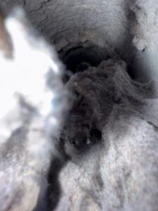 Inside view of a severely clogged dryer vent filled with thick layers of compacted lint and dust. The buildup covers the vent walls almost completely, blocking airflow and creating a significant fire hazard.